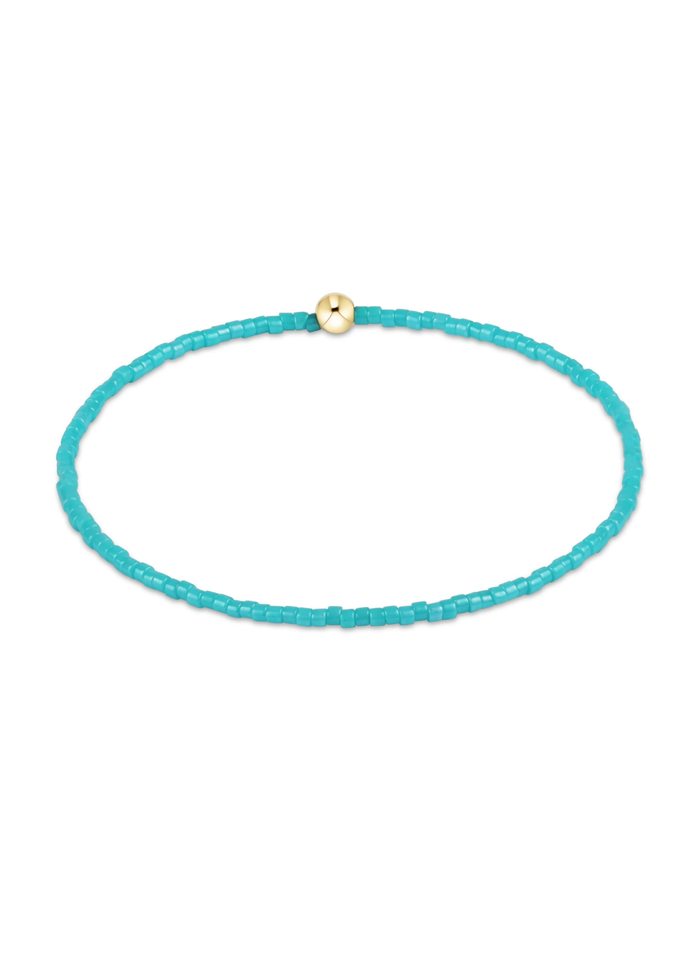 Turquoise beaded bracelet with one gold bead on a white background