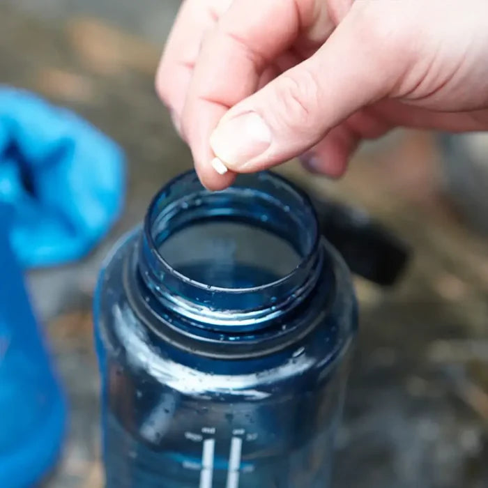 Person placing a Lifesystems Chlorine Water Purification tablet into a water bottle