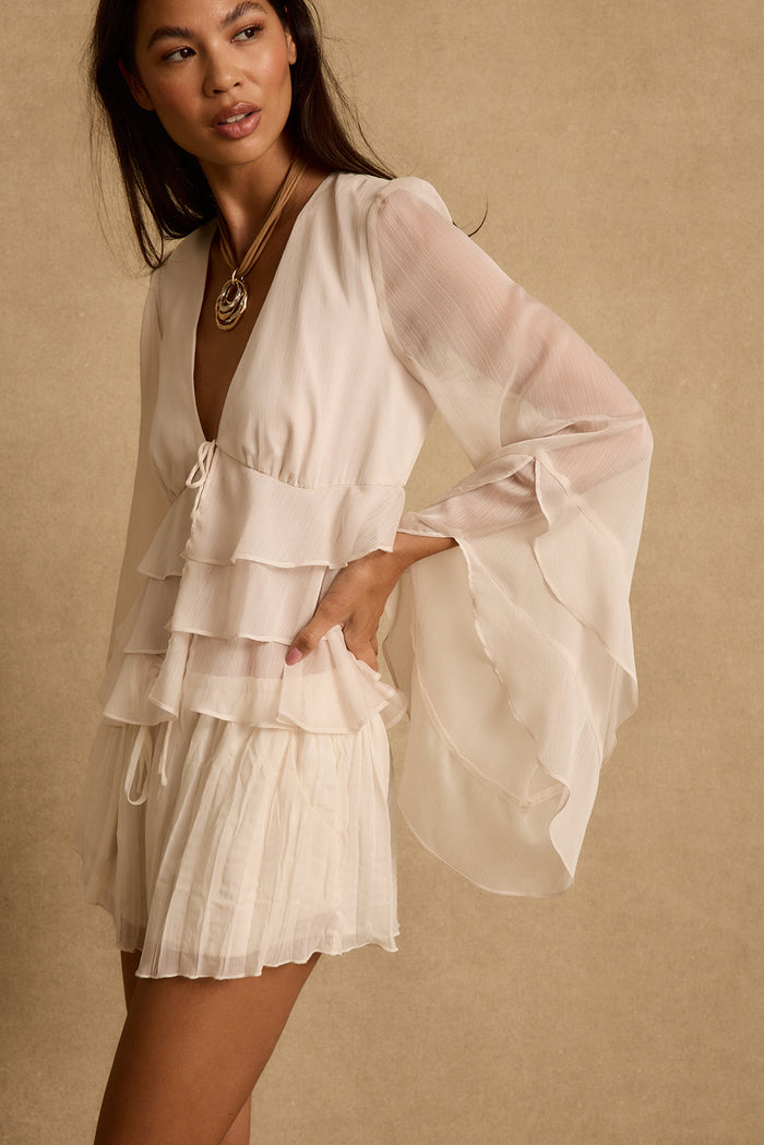 Sheer tulip bell sleeve drapes wide on the cream tiered ruffle blouse, styled with ivory shorts.