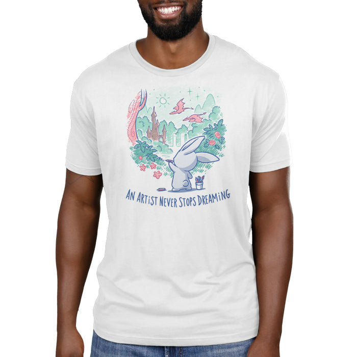 Premium Cotton T-shirt_TeeTurtle white An Artist Never Stops Dreaming apparel  featuring a bunny drawing a whimsical landscape with a castle, trees, and flying dragons. Caption reads, "an artist never stops dreaming".