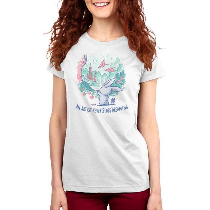 Premium Cotton T-shirt_TeeTurtle white An Artist Never Stops Dreaming apparel  featuring a bunny drawing a whimsical landscape with a castle, trees, and flying dragons. Caption reads, "an artist never stops dreaming".