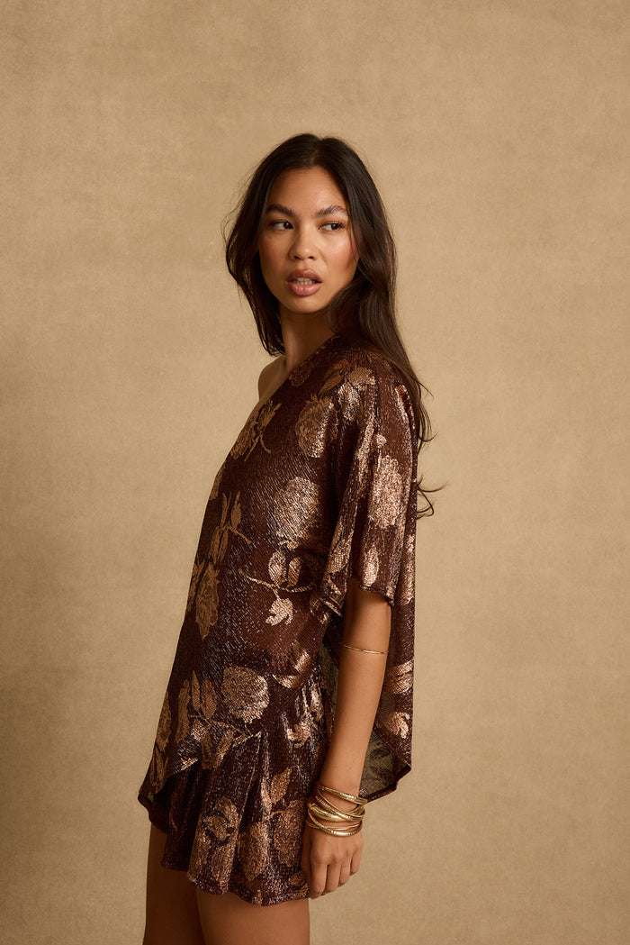 Side view of the shimmery mocha floral one shoulder top styled with matching shorts.