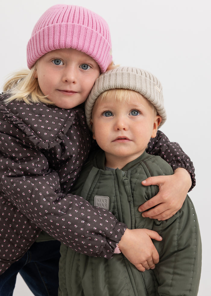 Two children wearing pink knitted hats and gray hats; pink ribbed knit with a round top.
