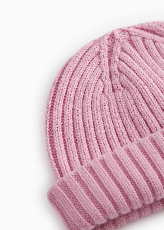 Pink knit cap shown in close-up: cable/knit stitch pattern and rib edge.