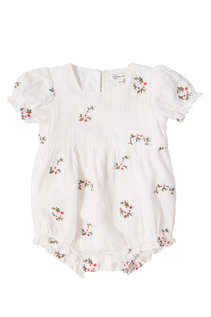 Dress your little one in the Baby Jessie Romper in Ditsy Embroidery by Ivy City Co. This white romper features short puff sleeves, subtle vertical stripes, and a charming embroidered pattern of small pink and green flowers. The smocked bodice lends classic detail, while elastic leg openings and sweet ruffles provide a soft, adorable touch. Made from comfortable embroidered cotton and photographed on a plain background for a clear view of its delightful design.