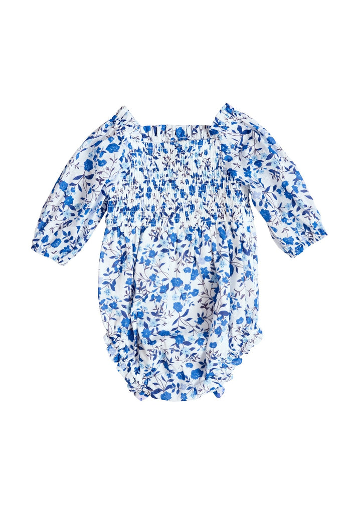 The Ivy City Co Baby Madeline Romper in Ditsy Cobalt Floral features a blue and white floral pattern, long sleeves with elasticized cuffs, and a smocked bodice, shown on a white background.