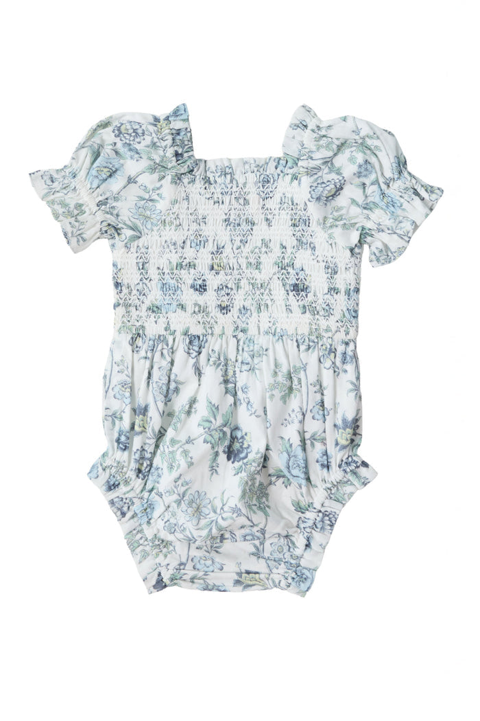 The Baby Valencia Romper in Ivory Climbing Vine Bloom by Ivy City Co is a charming cotton romper featuring short puff sleeves and a beautifully smocked bodice. The delicate blue and green floral design stands out against the crisp white background, making it perfect for both special occasions and everyday wear.