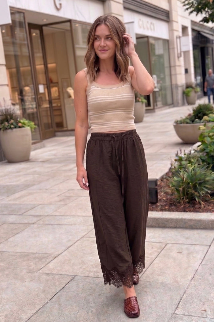 Brown lace trim barrel-leg pants featuring a relaxed wide-leg fit, elastic drawstring waistband, and intricate lace hem detailing, styled with a neutral striped tank and jelly flats.