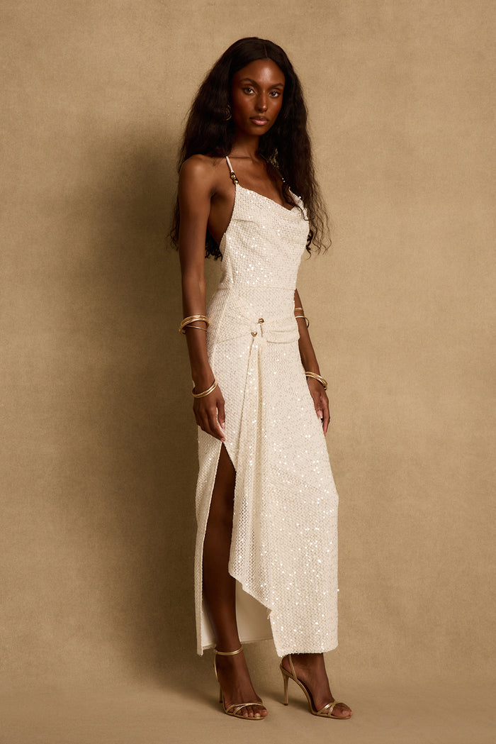 Cream sequin maxi dress with cowl neckline and side leg slit, styled with gold heels.