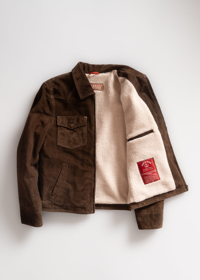 Brown suede jacket with a soft white fleece lining, open to reveal a red label inside. Features chest and side pockets.