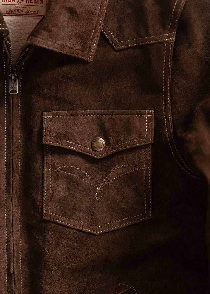 Close-up of a brown suede jacket with a buttoned pocket and visible stitching, showcasing Iron & Resin's premium craftsmanship.