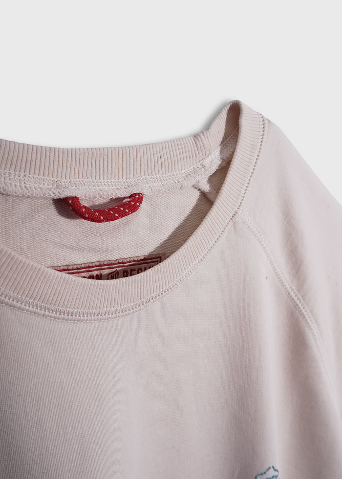 Close-up of a beige sweatshirt with a visible red label and loop inside the collar, highlighting its simple, casual design.