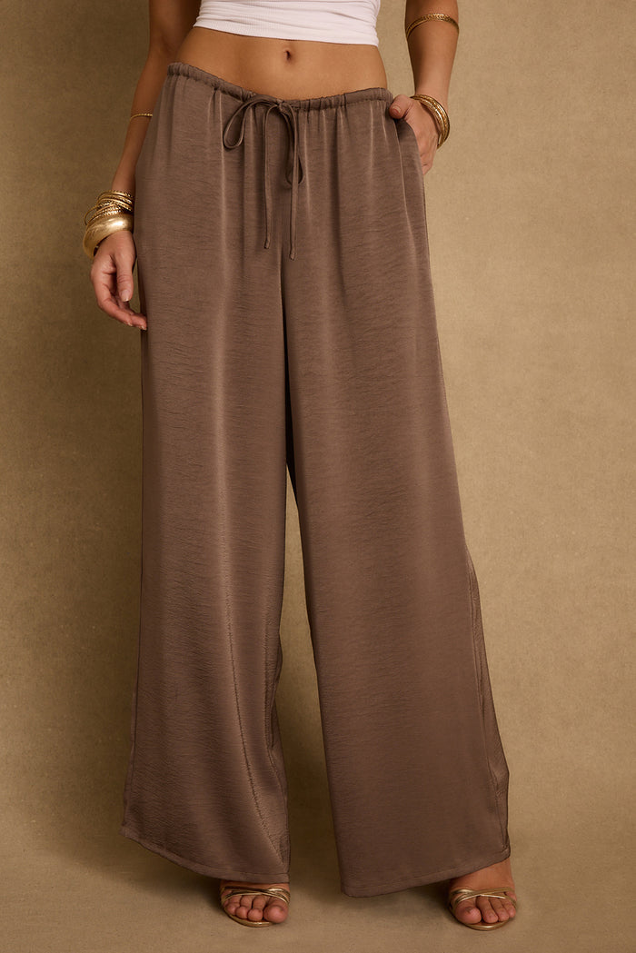 Taupe satin wide-leg drawstring pants styled with gold bangles and metallic heeled sandals.