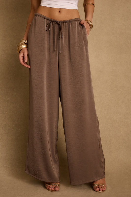 Taupe satin wide-leg drawstring pants styled with gold bangles and metallic heeled sandals.