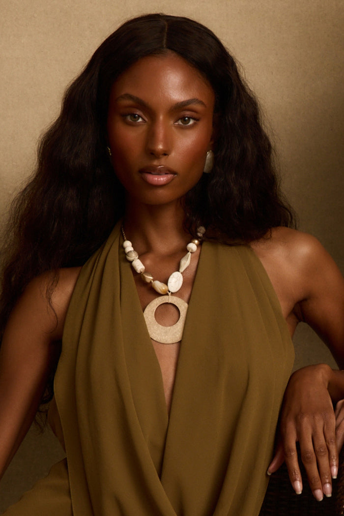 Beaded statement necklace with a large open-circle pendant styled over an olive halter dress.