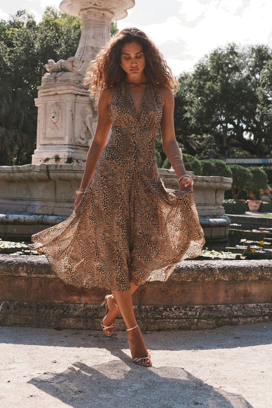 Darcy leopard print halter maxi dress worn with gold heels beside a garden fountain.