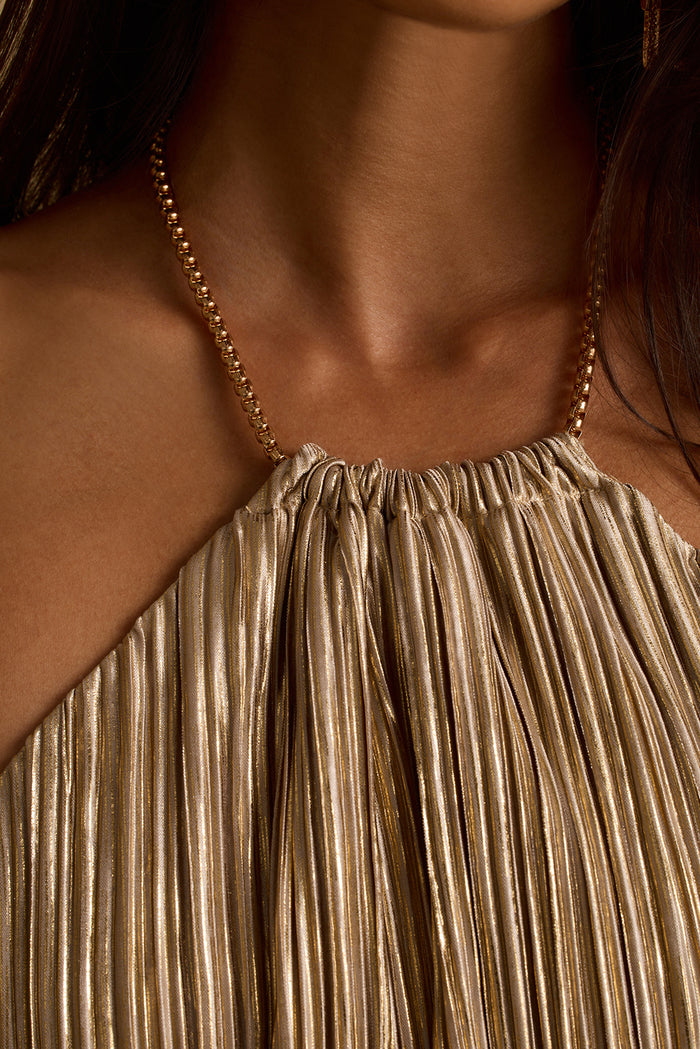 Close-up of rose gold chain halter neckline on a shimmering gold plisse party dress.
