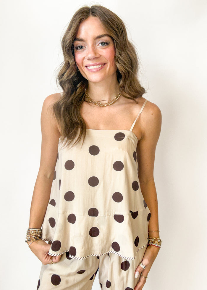 Woman wearing a beige tanktop with brown polka dots against a plain background