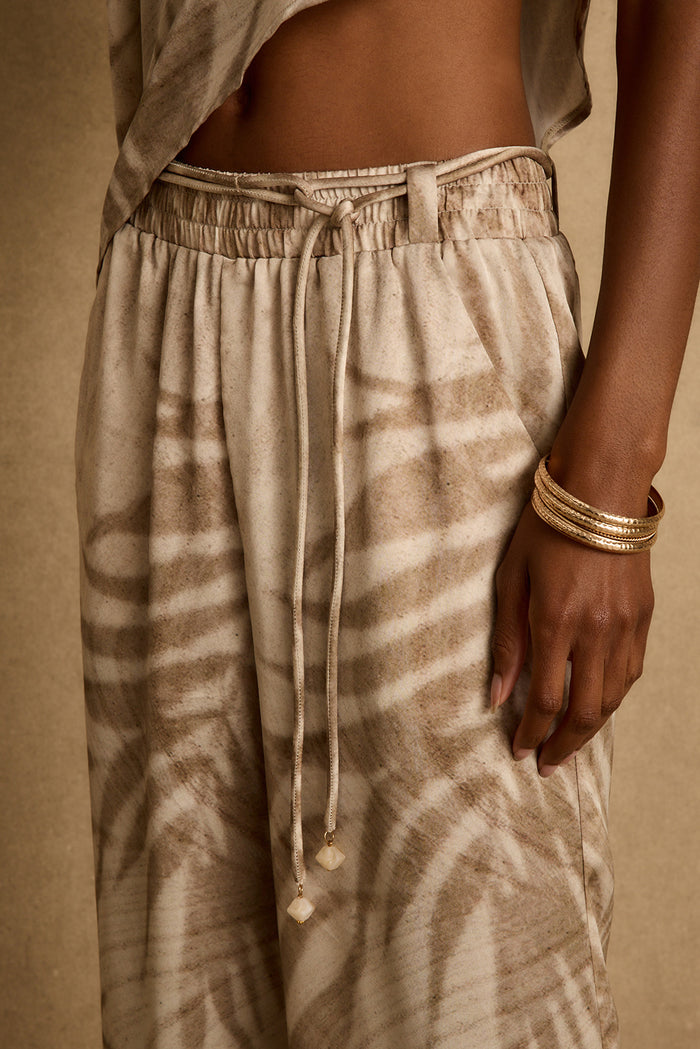 Close-up of neutral palm print satin pants with elastic waist and tie belt.