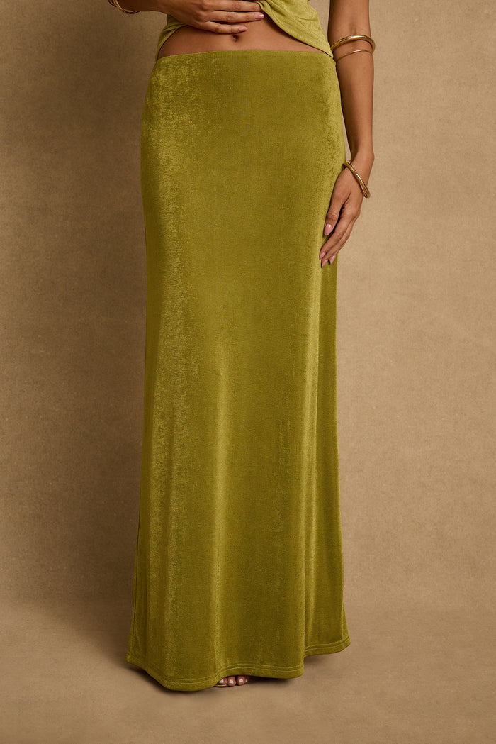 Close-up of chartreuse velvet maxi skirt skimming the floor, styled with gold bangles.