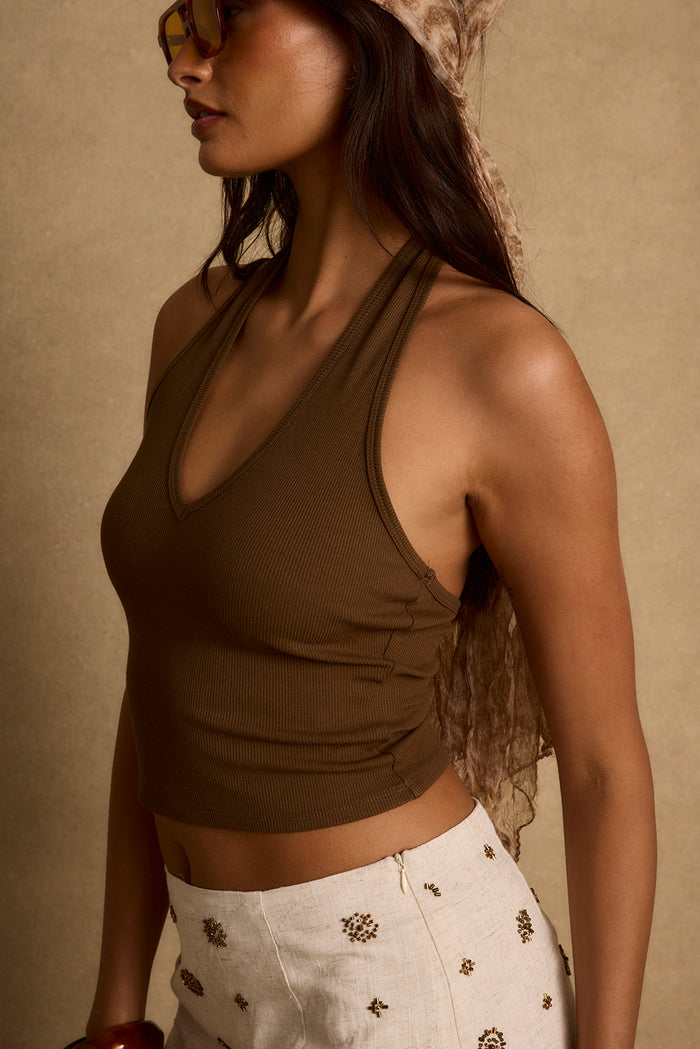 Side view of the ribbed mocha halter crop top styled with an embellished cream skirt.