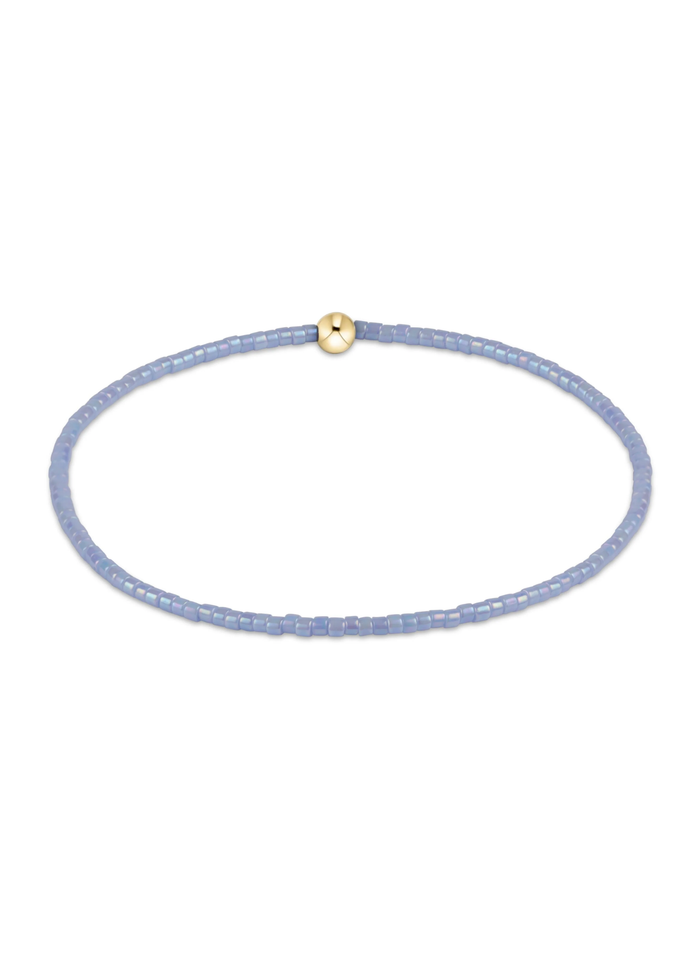 Light blue beaded bracelet with one gold bead on a white background