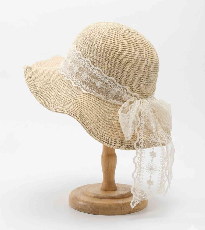 Beige straw wide-brim sun hat on stand with white lace ribbon and bow