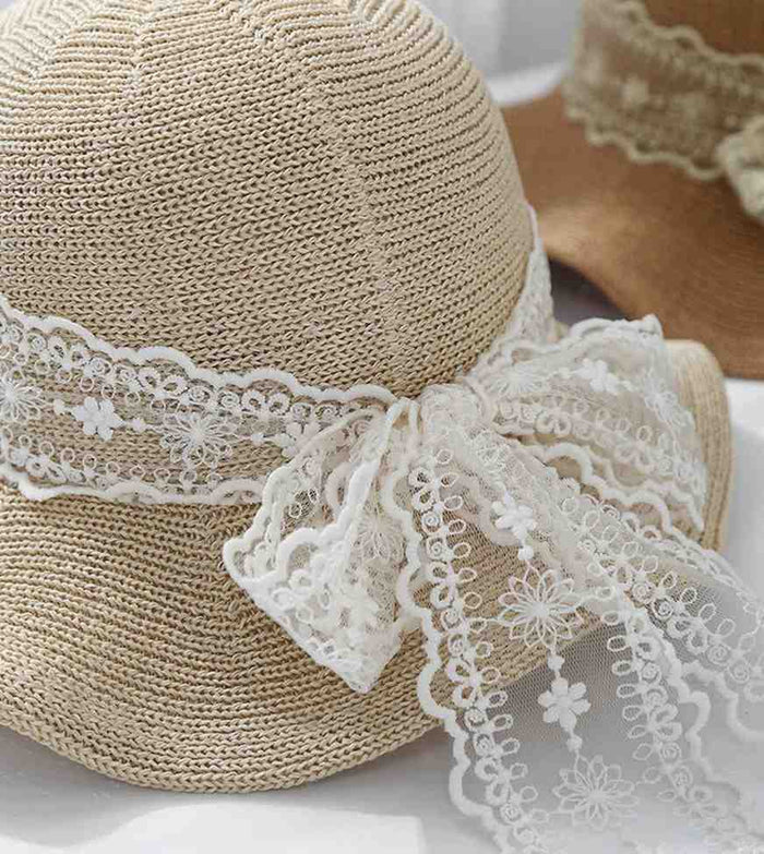 Beige straw sun hat close-up with white lace trim band and bow