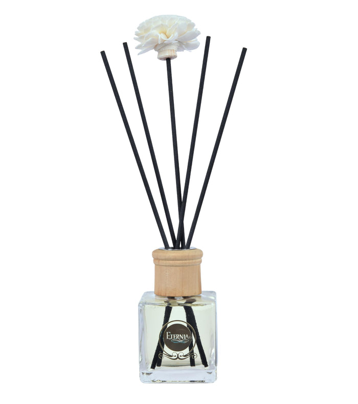 Reed diffuser glass bottle with light wooden cap and dark reeds, white flower topper