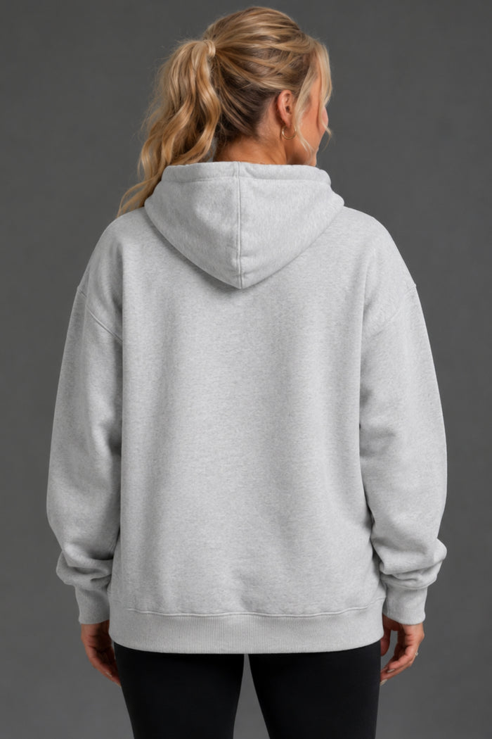 A woman viewed from the back wearing an oversized light gray heather pullover hoodie with black pants, set against a solid dark gray studio background. || Light Heather Gray