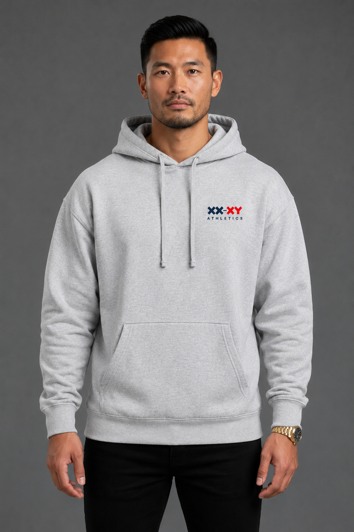 A man wearing a light gray heather pullover hoodie with a small red, white, and blue 'XX-XY AFFECTION' chest graphic, posed against a solid dark gray studio background. || Heather Gray