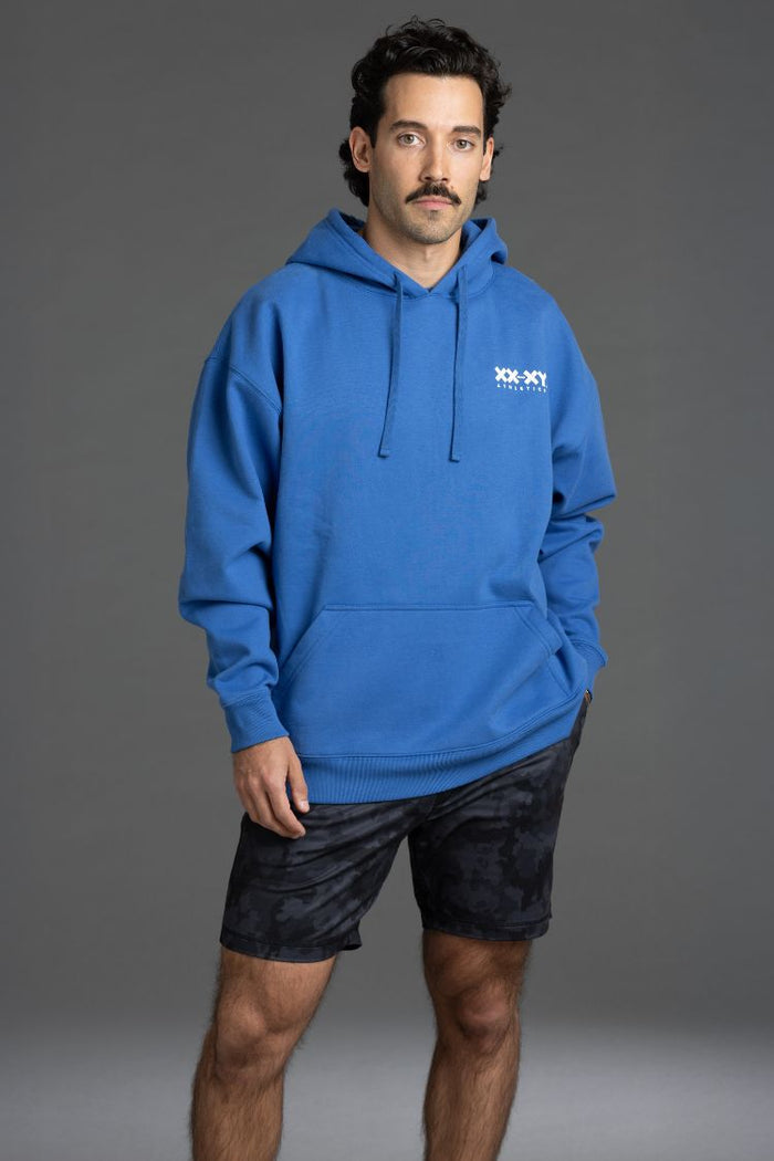 Man wearing a blue hoodie with a logo on a gray background || Blue
