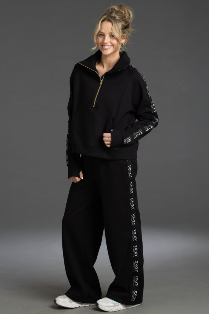 Woman wearing a black tracksuit with sequin details on a gray background || Black