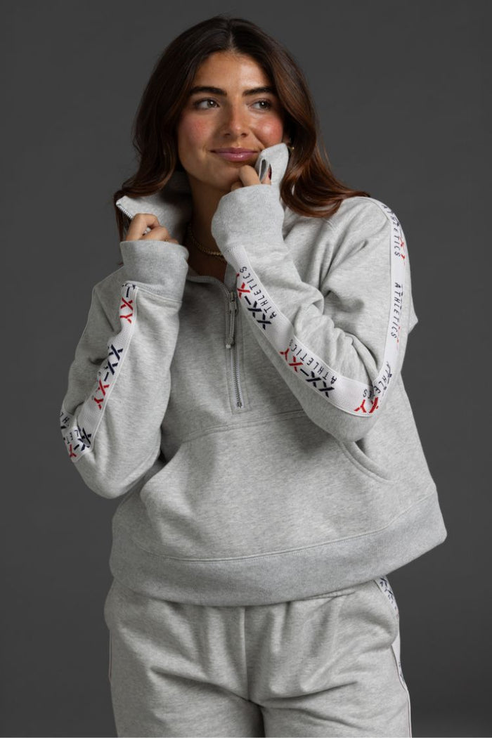 Woman wearing a gray hoodie and pants with embroidered sleeves against a dark background || Light Heather Gray