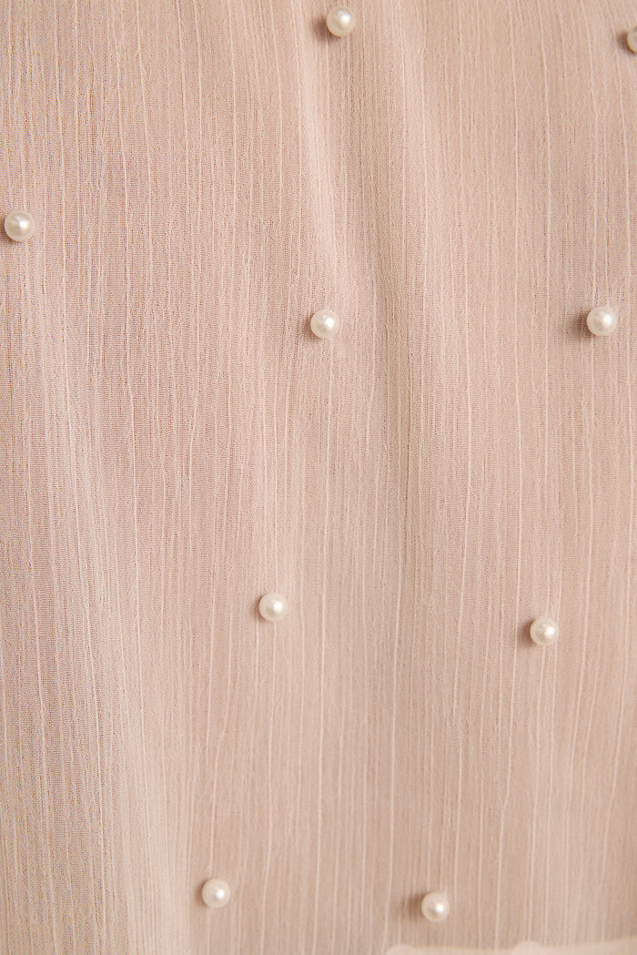 Ivory pearls scattered across sheer blush textured fabric of a pearl-embellished cape.