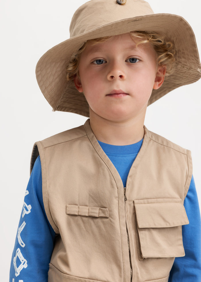 Sand-colored children's vest with snap pockets and zipper, worn by children with straw hats.