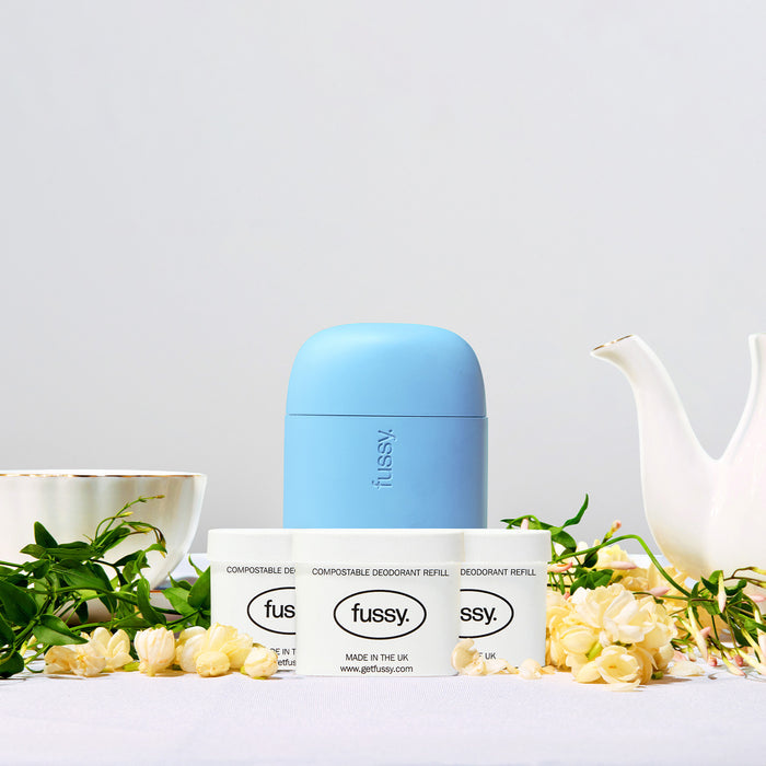 Fussy's Jasmine Bloom Refill Deodorant pack set against a backdrop of a teapot, teacup, jasmine flowers and foliage.