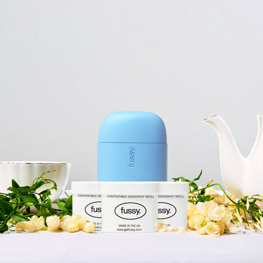 Fussy's Jasmine Bloom Refill Deodorant pack set against a backdrop of a teapot, teacup, jasmine flowers and foliage.