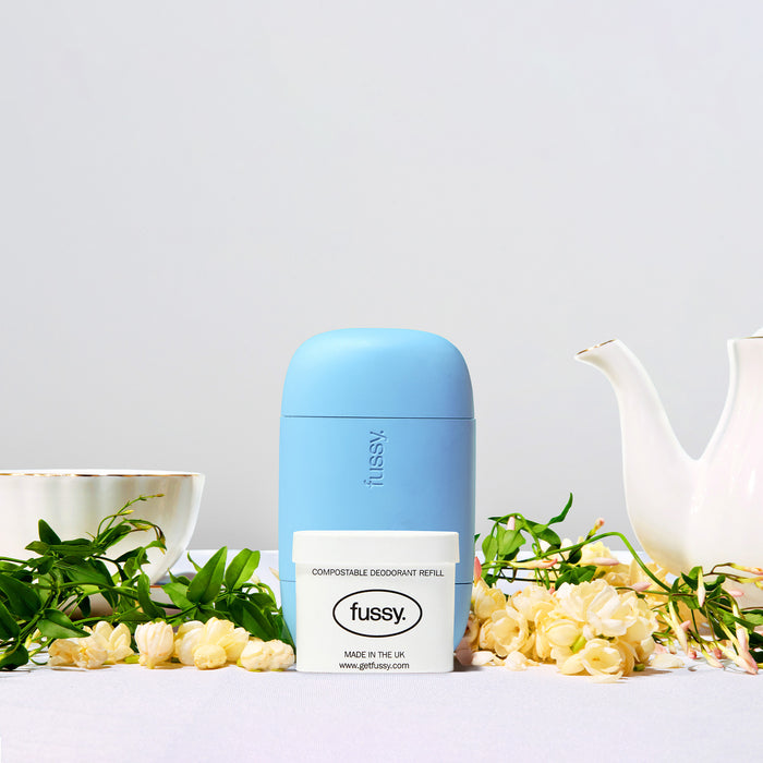 Fussy's Refillable Deodorant Starter Pack in Green Tea scent, surrounded by jasmine flowers, green leaves and teacups on a white background.