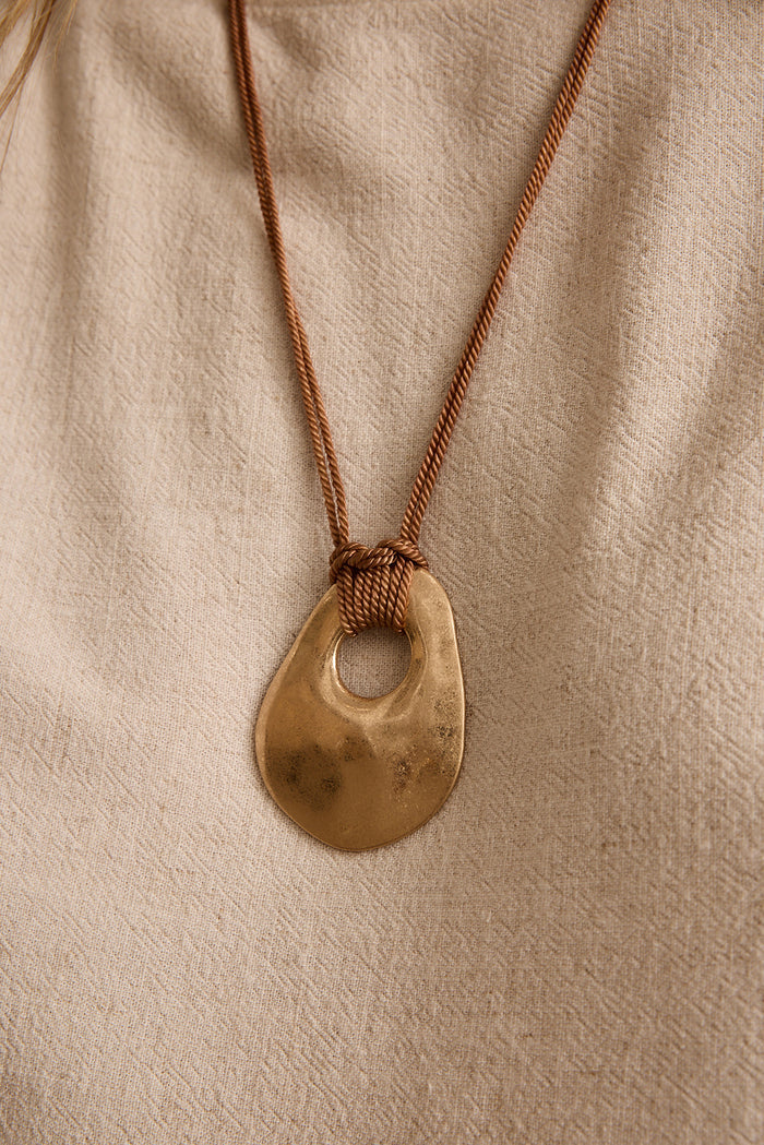Close-up of the Lani hammered gold pendant knotted on a brown woven cord.