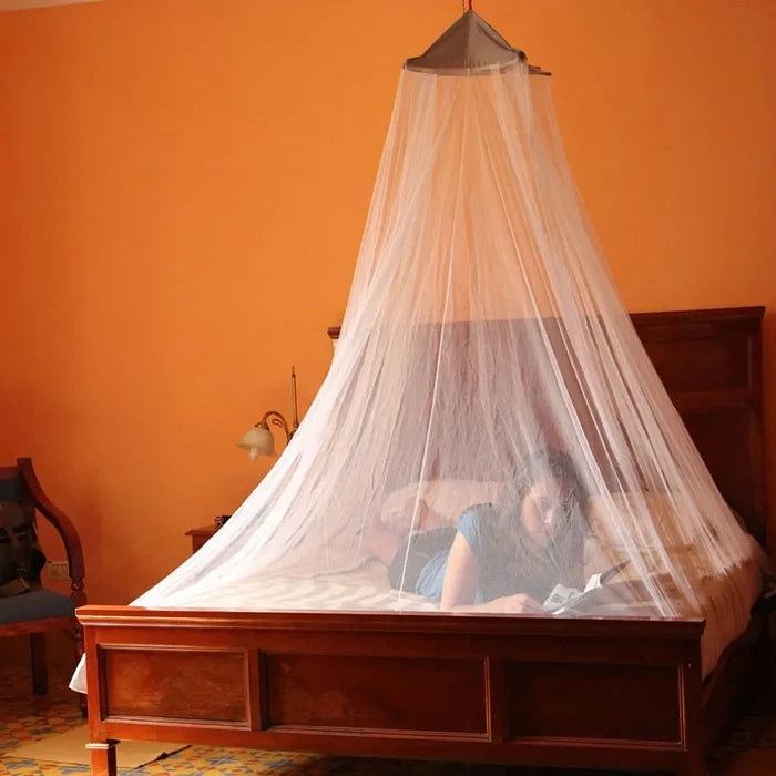 Person lying under a Lifesystems Bell Double Mosquito Net on a double bed with an orange wall in the background