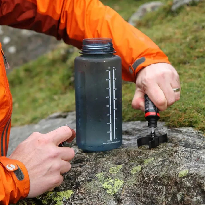 Person in an orange jacket mixing the Lifesystems Chlorine Dioxide Water Purification Drops before adding them to the water in the drinking bottle