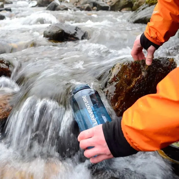 Person filling a water bottle from a babbling stream for use with Lifesystems Chlorine Dioxide Water Purification Tablets