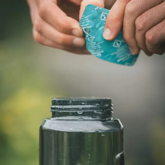 Person pushing out a Lifesystems Chlorine Dioxide Water Purification Tablet in to a bottle of collected water