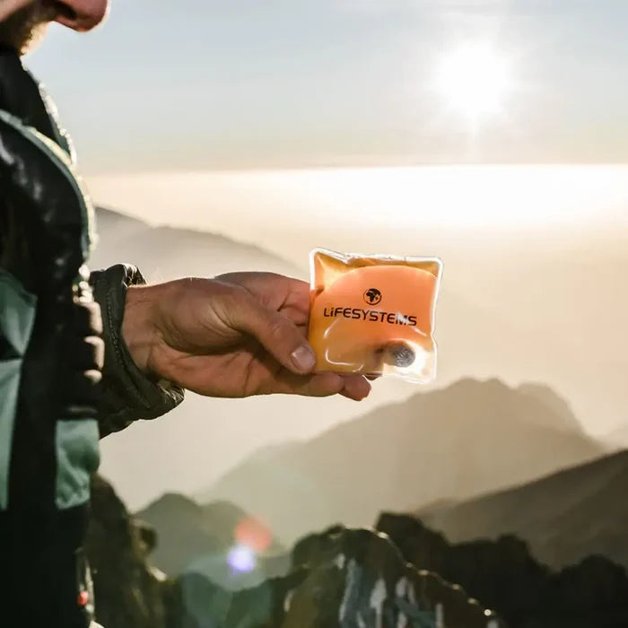 Person holding a Lifeventure reusable hand warmer against a mountainous landscape
