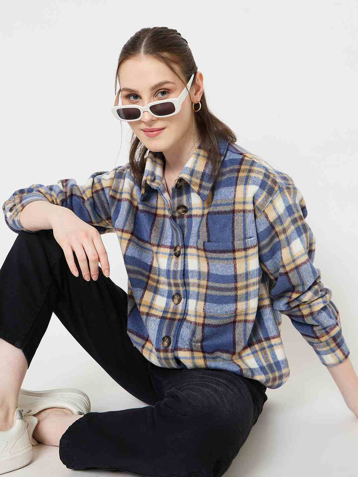 Woman wearing a blue and yellow plaid shirt sitting on the floor with a white background