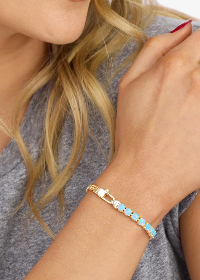 Woman wearing a gold chain bracelet with seven blue opals on a white background