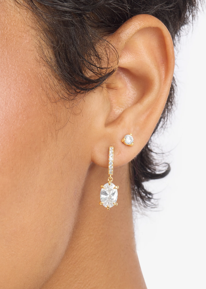 Woman wearing a pair of gold and simulated diamond huggie earrings