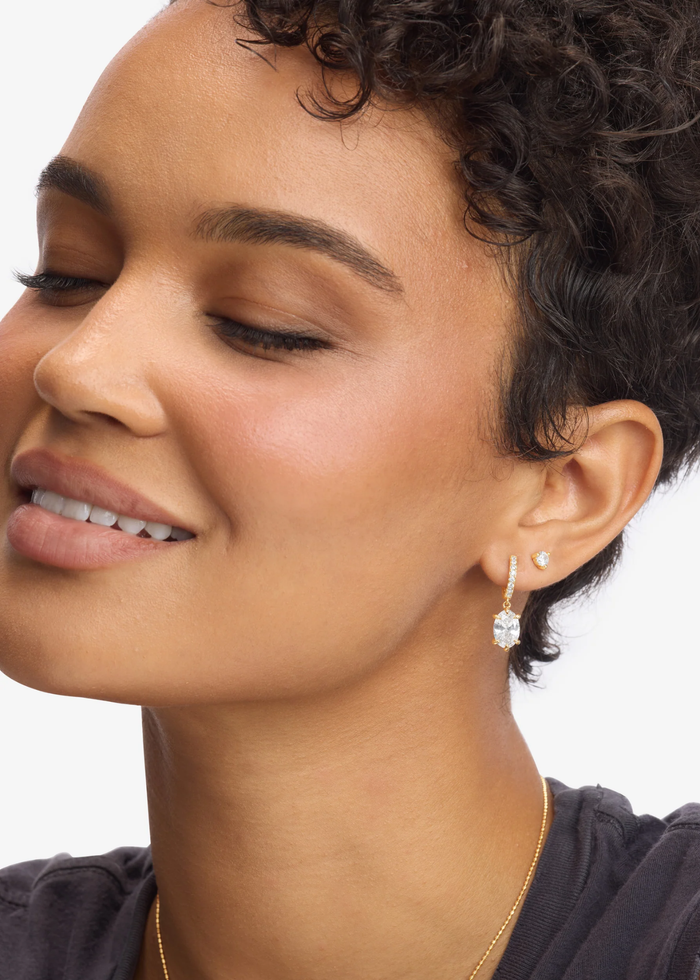 Woman wearing a pair of gold and simulated diamond huggie earrings