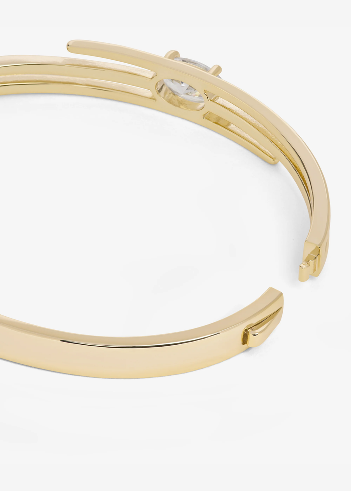 Close up of the clasp of a gold lasso cuff bracelet with a diamond stud against a white background